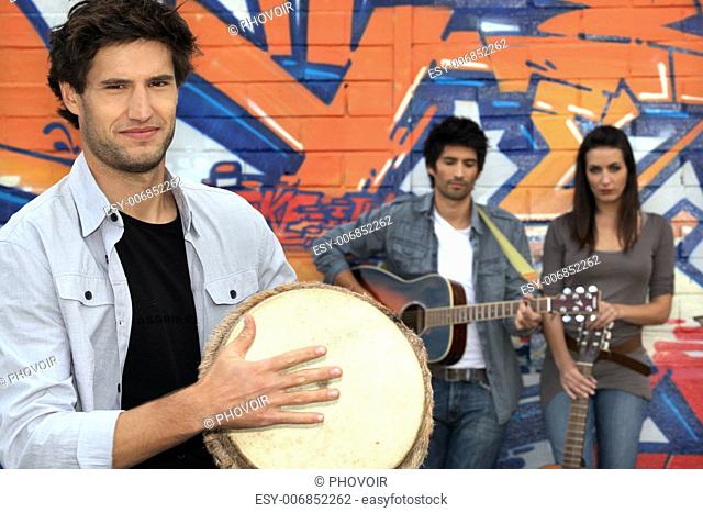 three musicians in front of a tagged wall