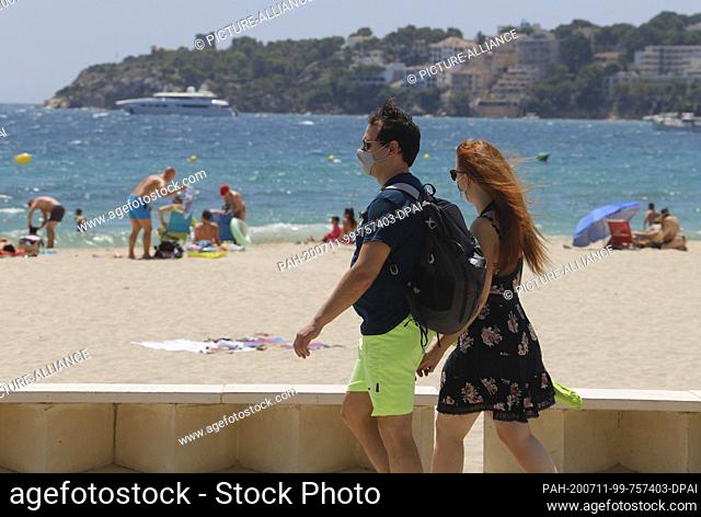 11 July 2020, Spain, Calvia: A young couple is taking a walk on Son Maties beach wearing mouth-nose masks. The regional government of the islands has announced...