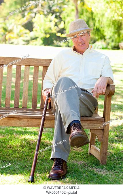 Man smiling while siting on a bench as he hold a cane