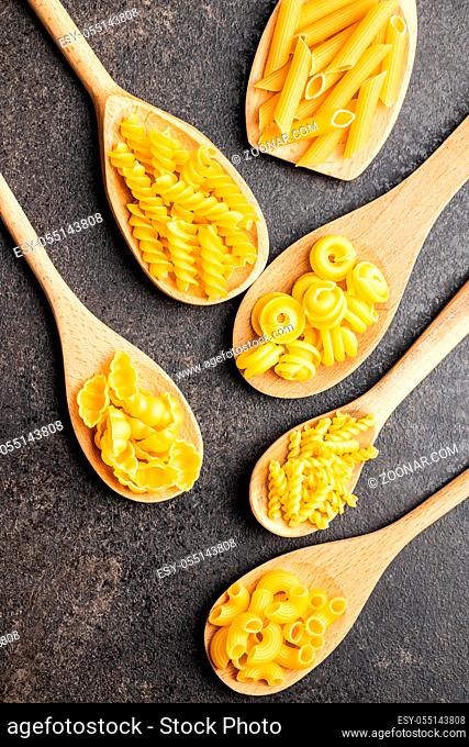 Various types of raw italian pasta in wooden spoons on black table. Top view