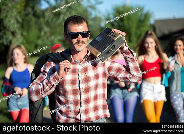 Funny man with a cassette recorder in front of a group of girls. People in the style of the nineties
