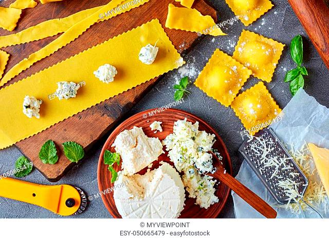 cooking up delicious ravioli with ricotta cheese filling mixed with finely chopped mint and basil leaves on a concrete kitchen table with ingredients