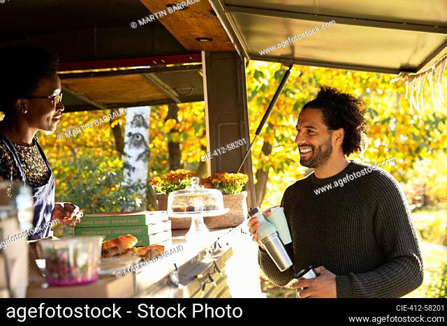 Happy customer talking with food cart owner in autumn park