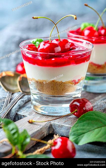 Homemade cheesecake with cherry jelly in a glass close-up and fresh cherries on a wooden serving board, selective focus