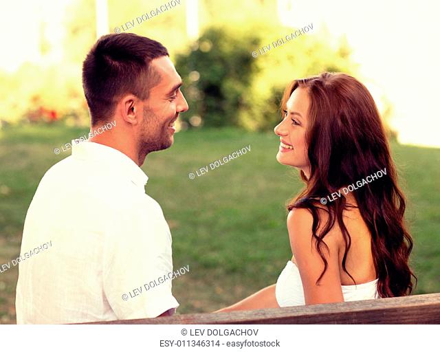 love, dating, people and friendship concept - smiling couple sitting on bench and looking to each other in park