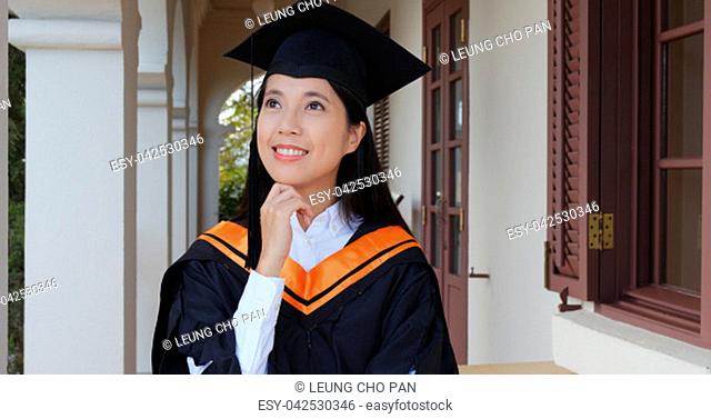 Woman wearing graduation gown and hold with certificate and look far away