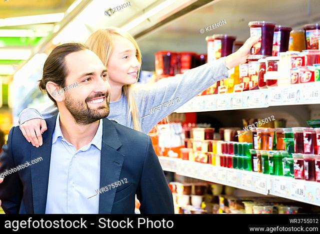 Father carrying daughter on his back while she is selecting dessert at grocery shopping in supermarket