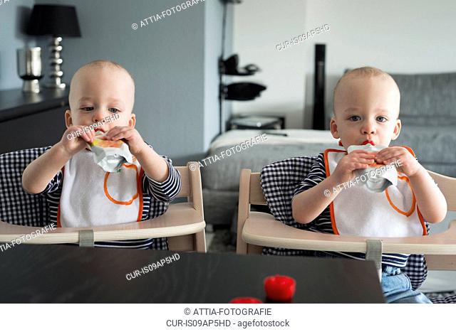 Baby twin brothers drinking juice in high chairs