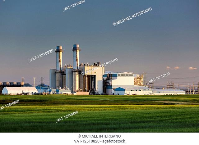 Large electrical generation plant at sunrise with blue sky and green grain field in the foreground, East of Calgary; Alberta, Canada