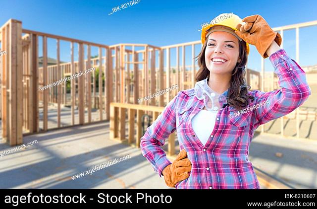 Young attractive female construction worker wearing gloves, hard hat and protective goggles at construction site