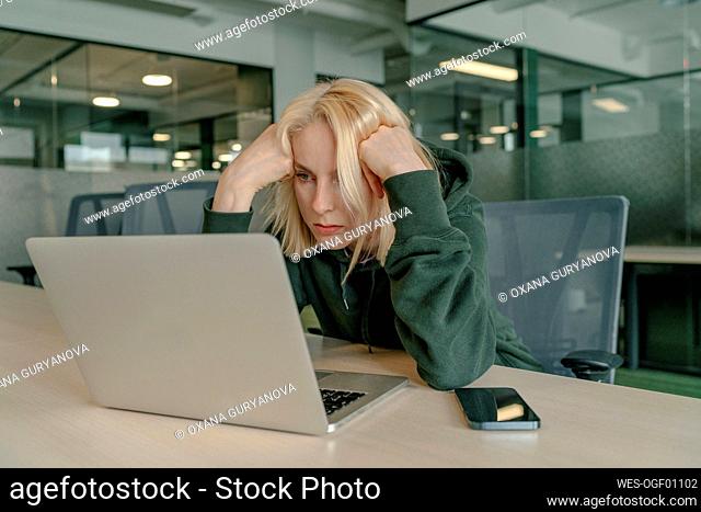 Frustrated businesswoman with head in hands looking at laptop in office