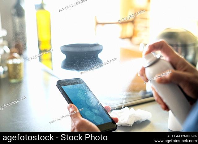 Close-up of woman's hands spraying disinfectant on smartphone at home