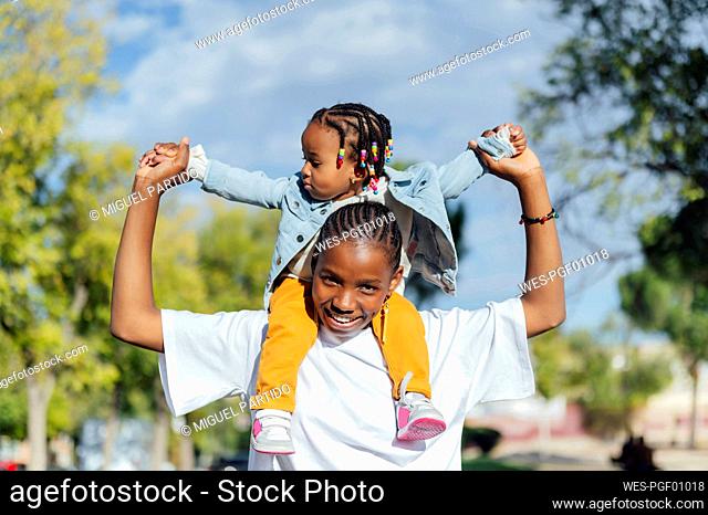 Happy woman carrying cute daughter on shoulders at park