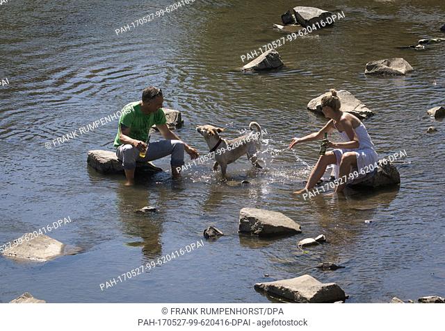Two day trippers sit on stones at the little Nidda River and sprinkle their dog with water in Bad Vilbel, Germany, 27 May 2017