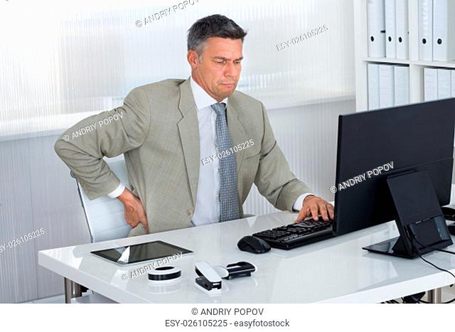 Mature businessman suffering from back pain at desk in office