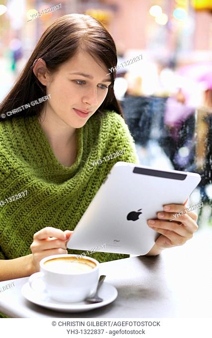 Young woman relaxing with her Cappuccino while browsing with her iPad outdoor