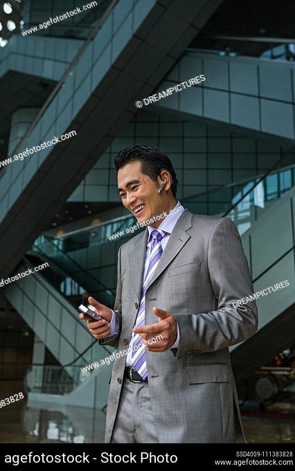 Chinese businessman talking on cell phone with hands-free device
