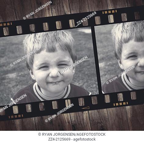 Vintage photo of an old film strip on a wooden table showing the face of a cute two year old child smiling for the camera wearing 2 jumpers during a British...