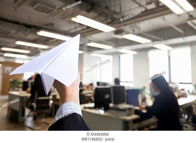 Hand holding paper airplane in office
