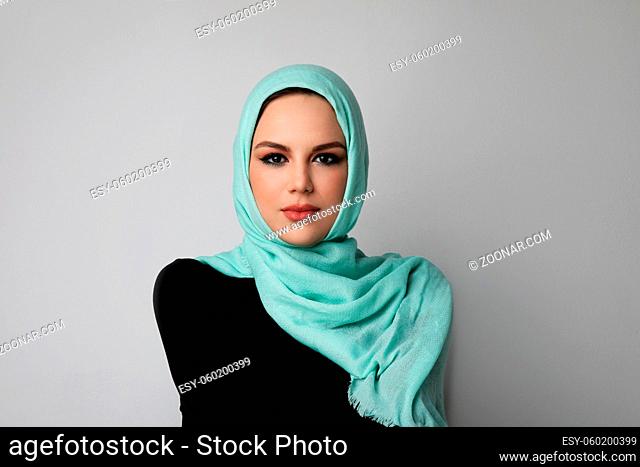 Vertical portrait of young muslim woman wearing green hijab. Light background. High quality photo