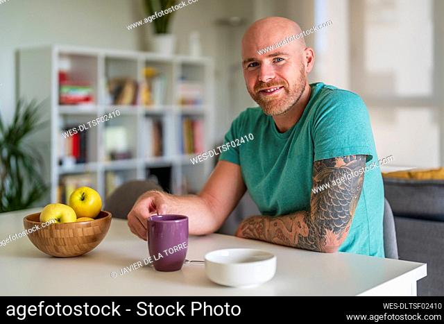 Smiling man with fruit and drink on table at home