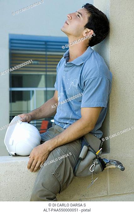 Man sitting on ledge, leaning head back, looking up