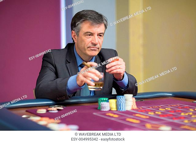 Man looking at the roulette table looking angry while holding a glass