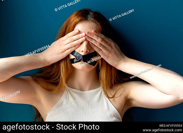 Portrait of young woman with taped mouth covering her eyes