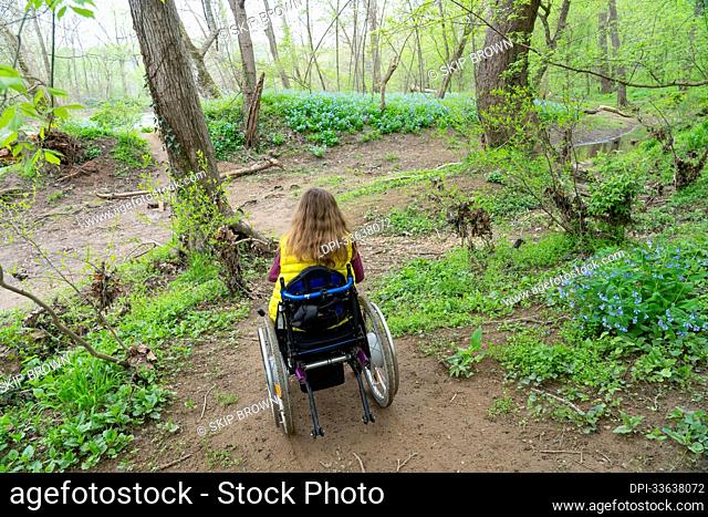 Girl in a wheelchair on a rugged path to explore wildflowers by the Potomac River; Cabin John, Maryland, United States of America