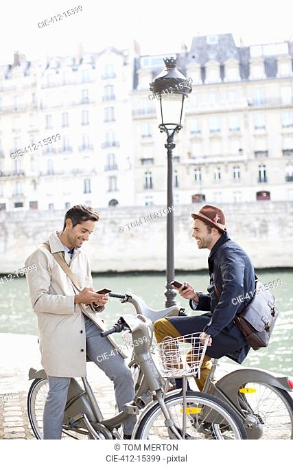 Businessmen with cell phones on bicycles along Seine River, Paris, France