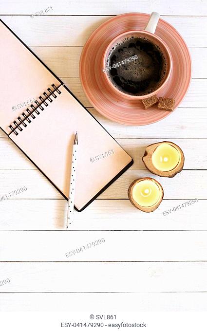 Blank notepad with pen, cup of coffee and candles on white desk. Top view point, flat lay