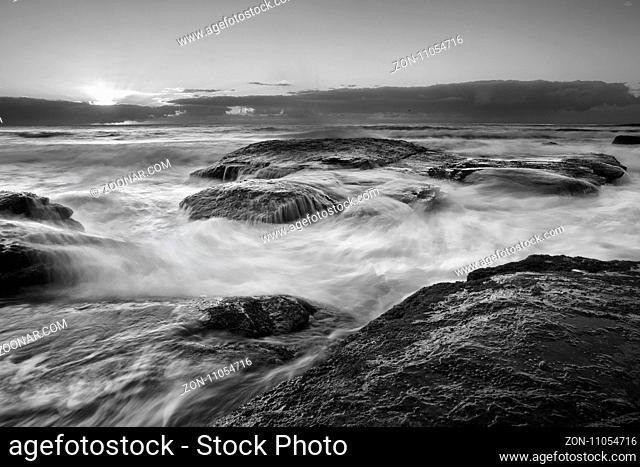 Rocky coastline with ocean surges and whitewater flows. Black and white. Location Bungan beach Australia