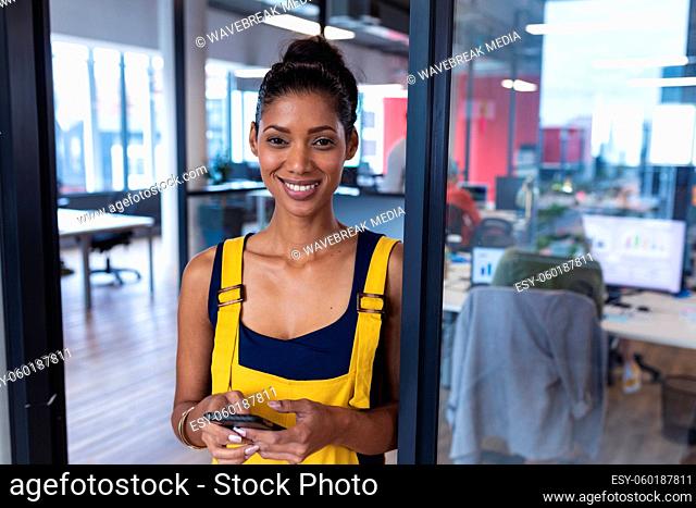Portrait of mixed race female creative worker using smartphone and smiling