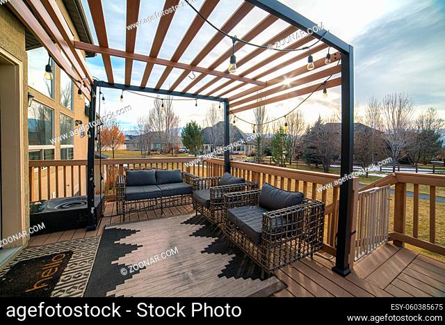 Wooden pergola over an exterior patio with garden furniture and a banister overlooking a large back yard