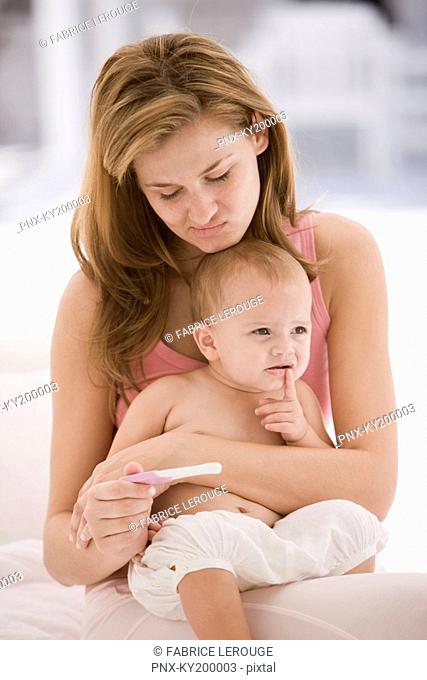 Woman looking at a pregnancy test stick with a her daughter sitting on her lap