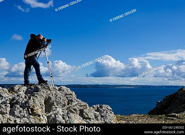 Outdoor photographer standing on a rock and taking photos of the breathtaking landscape of Brittany near Pointe de Penhir