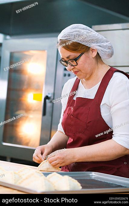 Adult woman in glasses and apron bakes cakes in the bakery half-profile smiling close-up