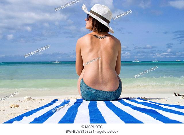 topless woman with sun hat, sitting on the beach on a striped towel, Philippines