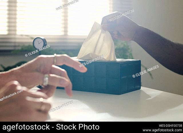 Hand of patient pulling paper napkin from box at desk in office