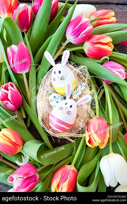 Kleines Osternest mit bunten Eiern und Tulpen
