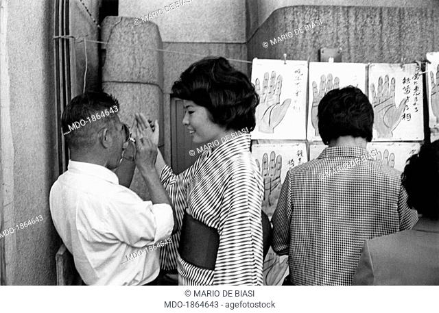 A palmist reading the palm of a Japanese girl. Tokyo, October 1964