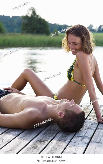 Young couple relaxing on jetty beside lake