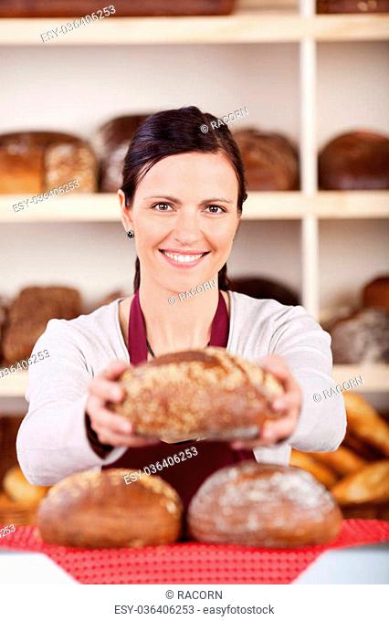Friendly female bakery assistant or worker with a beautiful smile standing behind a counter holding a loaf of rye bread in her hands with focus to her face