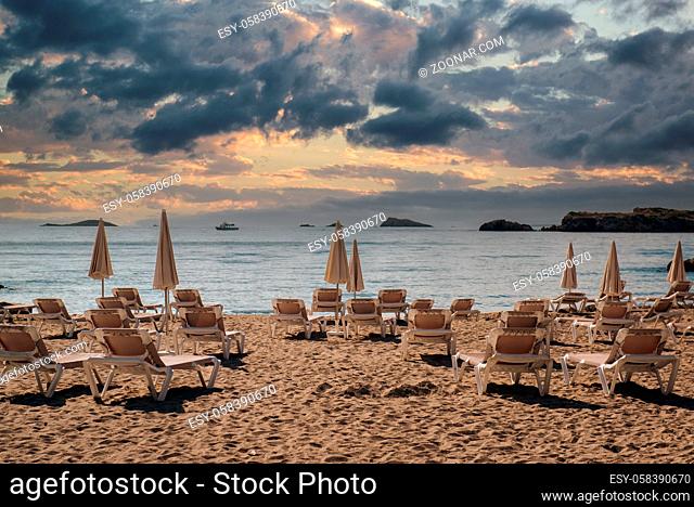 Empty beach at sunset. Folded parasols deck chairs on the beach of Ibiza during sundown, Balearic Islands. Spain. Beauty in nature
