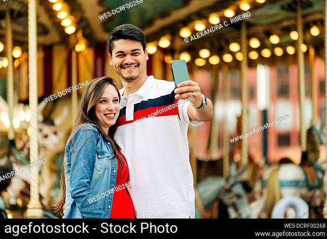 Happy expectant couple taking selfie through smart phone at amusement park, Cascais, Portugal