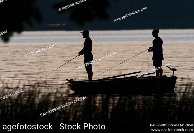 16 August 2022, Schleswig-Holstein, Eutin: 16.08.2022, Eutin. Two young men fish from a boat in the Kellersee in the backlight of the evening sun