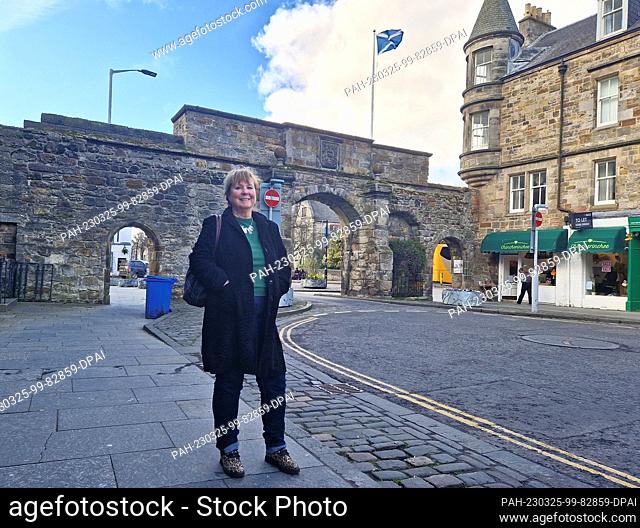 24 March 2023, Great Britain, St. Andrews: Independence activist Jane Philips from Dundee stands in front of an archway and a Scottish flag in the Scottish town...