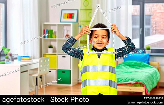 little boy in safety vest with house made of ruler