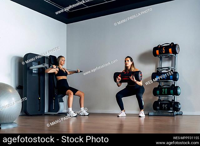 Female athletes lifting punching bag and doing suspension training in gym
