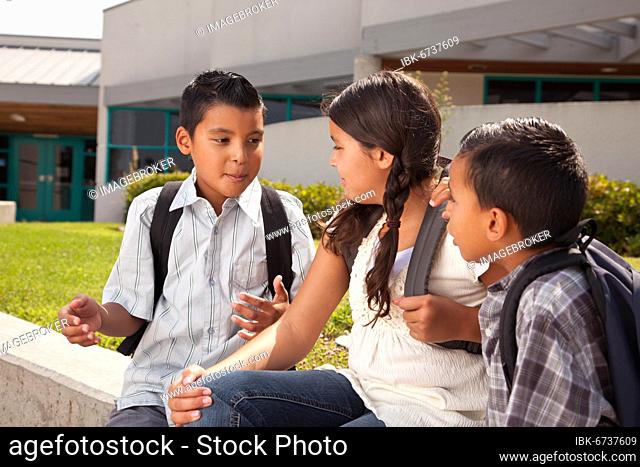 Cute brothers and sister talking, wearing backpacks ready for school